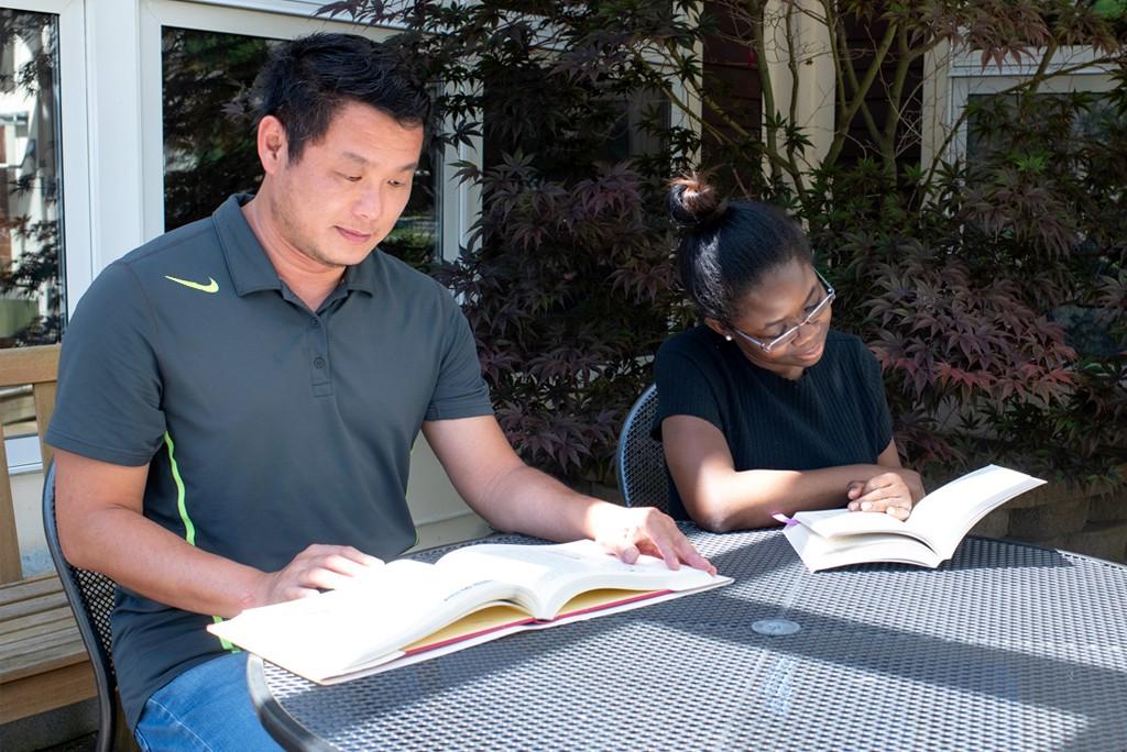 Two U N E students sit together at an outside table each reading a textbook