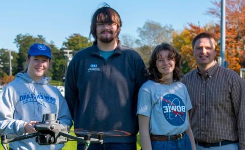 A faculty member and three students pose with a flying drone