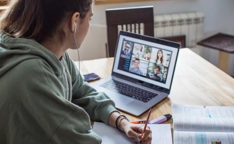 A young woman studying over a video call at a kitchen table